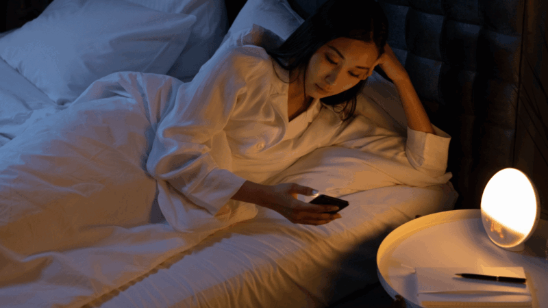 Image montrant une femme sur son teléphone portable le soir dans son lit ce qui est fortement déconseillé pour mieux dormir